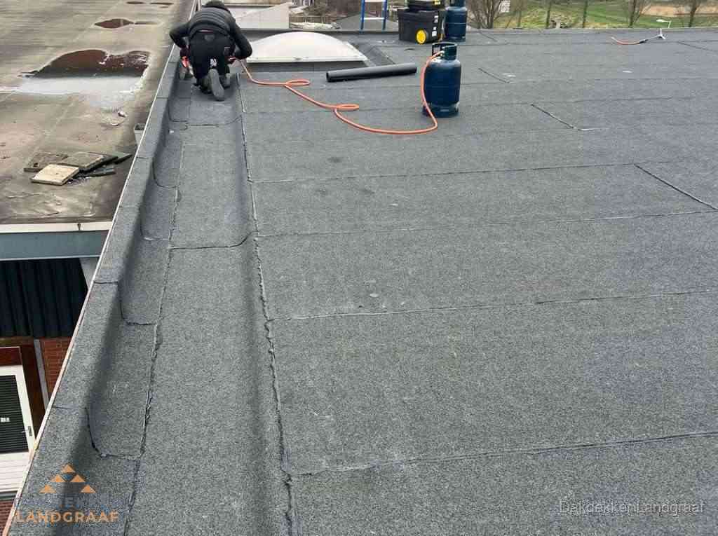 Dakdekker repareert bitumen dakbedekking op groot plat dak in Landgraaf Dakdekker repareert bitumen dakbedekking op groot plat dak in Landgraaf